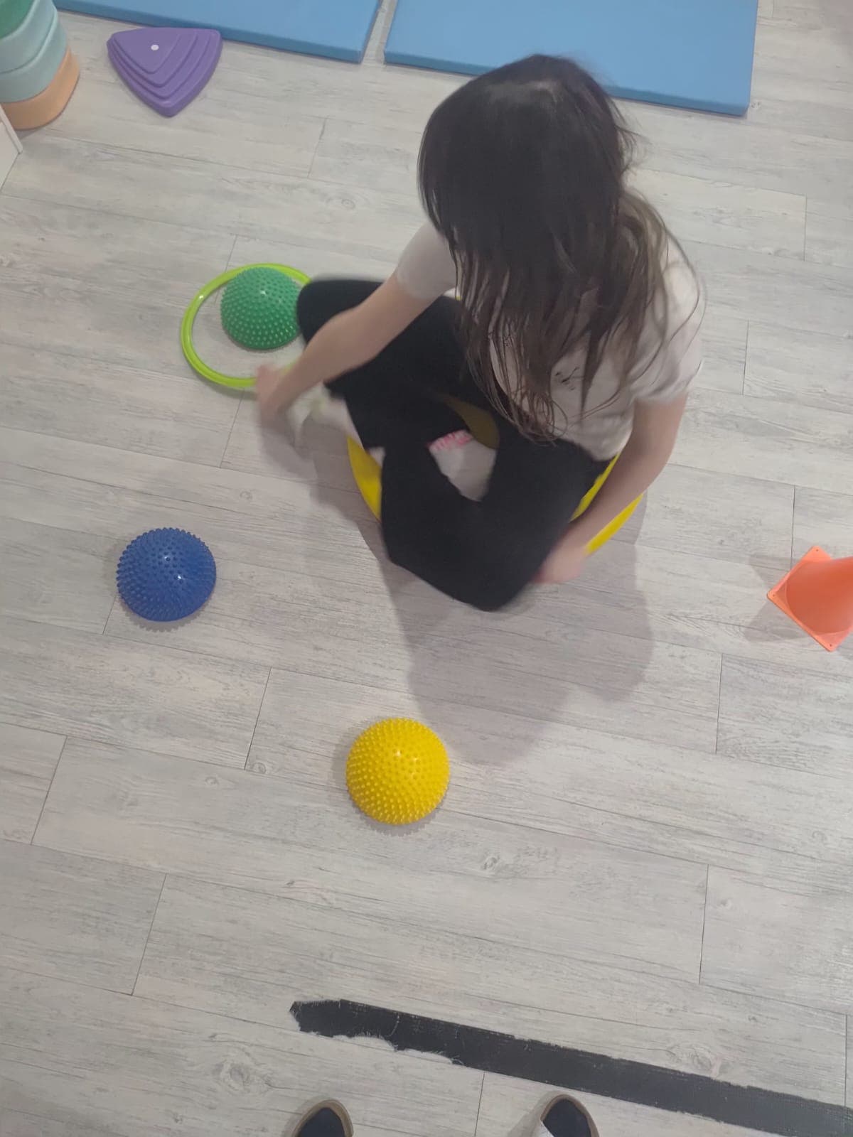 Dziecko wykonuje ćwiczenie równoważne z wykorzystaniem pomocy terapeutycznych.