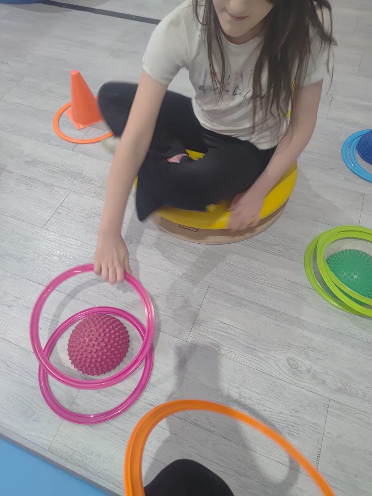 Dziecko wykonuje ćwiczenie równoważne z wykorzystaniem pomocy terapeutycznych.