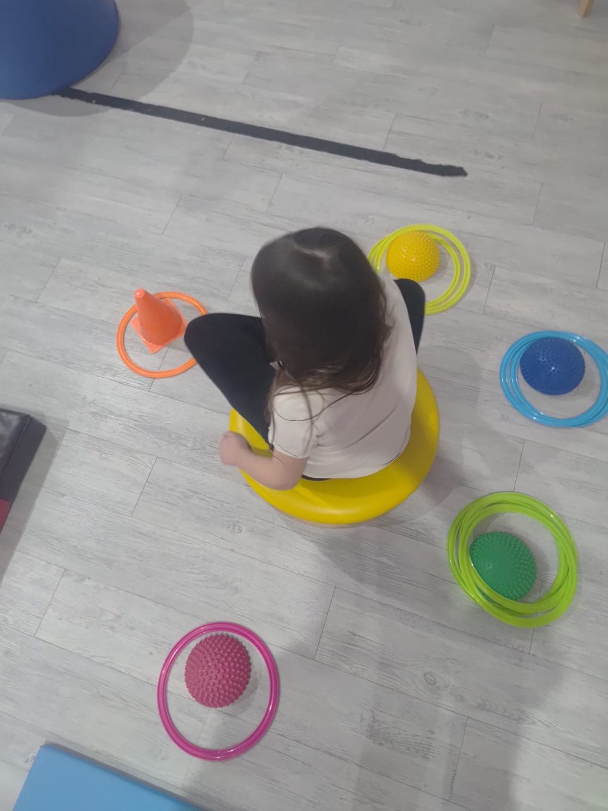 Dziecko wykonuje ćwiczenie równoważne z wykorzystaniem pomocy terapeutycznych.