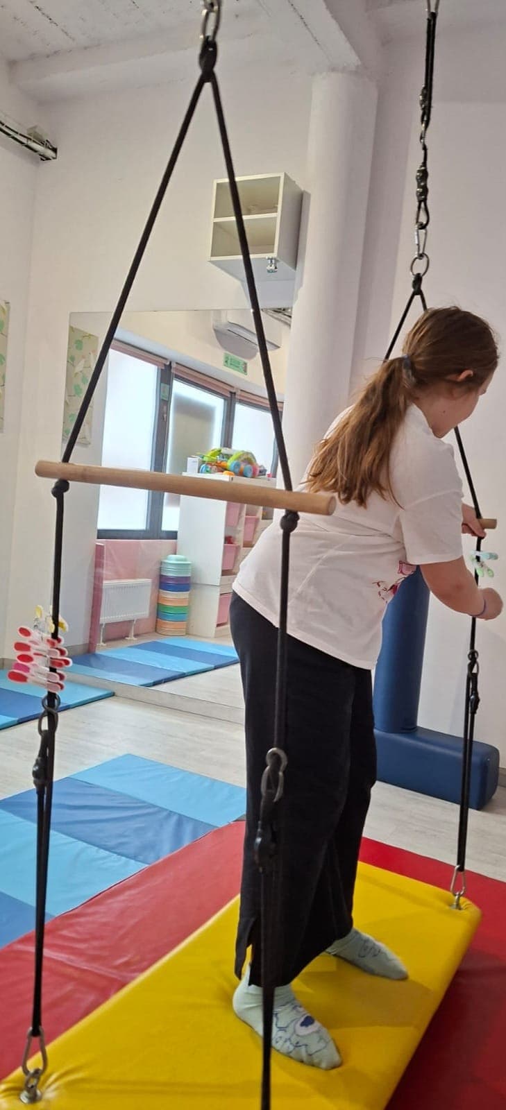 Dziecko wykonuje ćwiczenie równoważne z wykorzystaniem pomocy terapeutycznych.