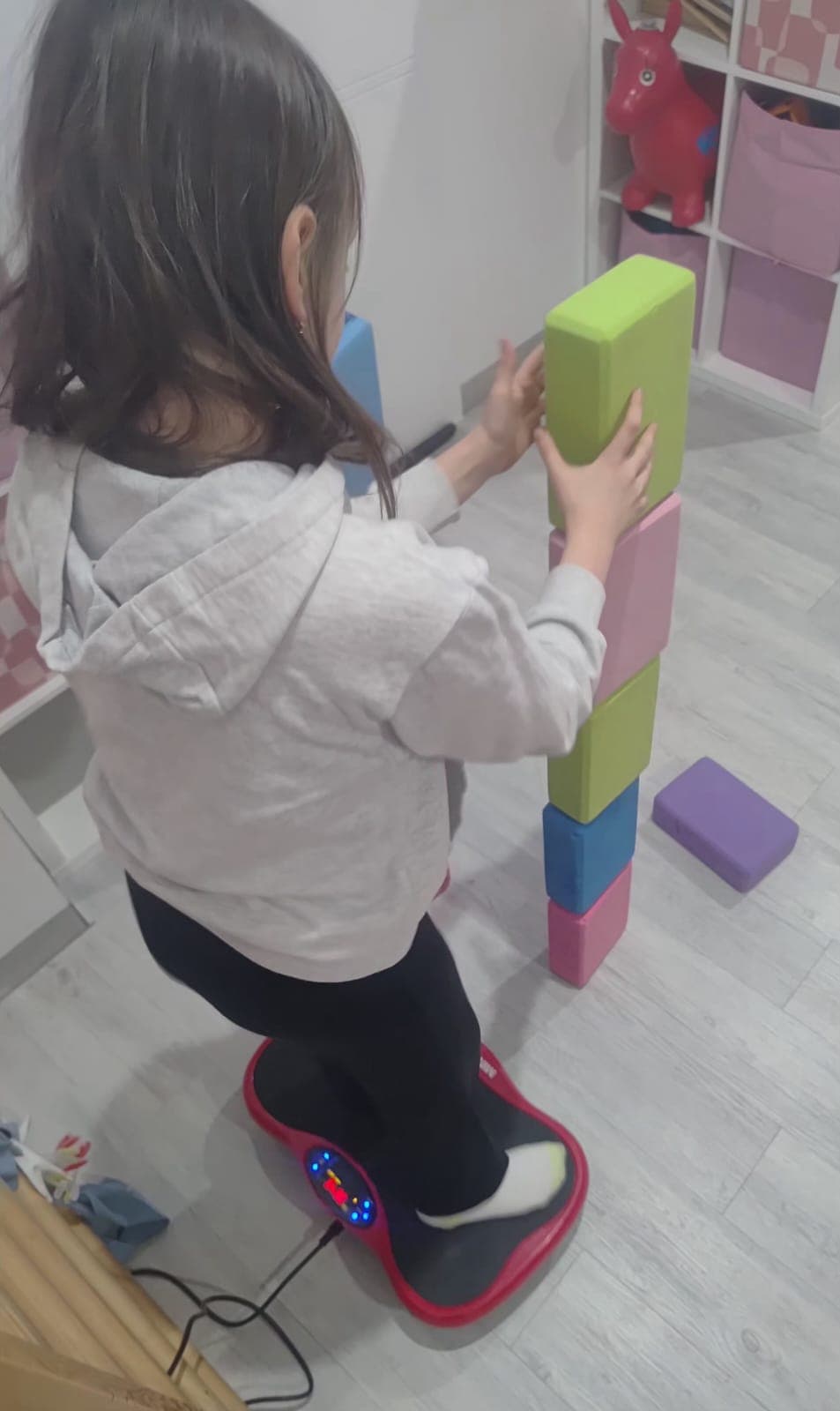 A child performs an exercise on a vibration platform during therapy.