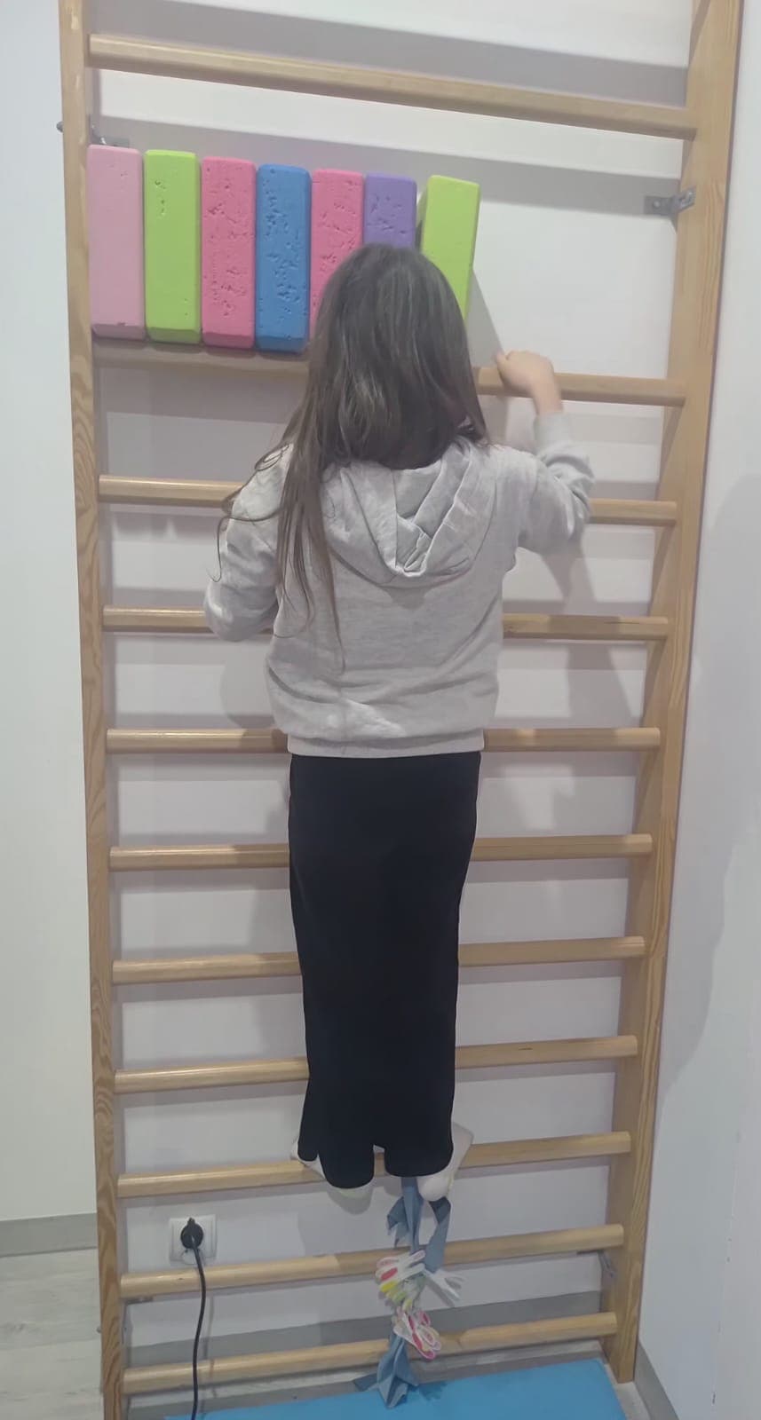 Dziecko wykonuje ćwiczenie ruchowe przy drabince w sali terapeutycznej.