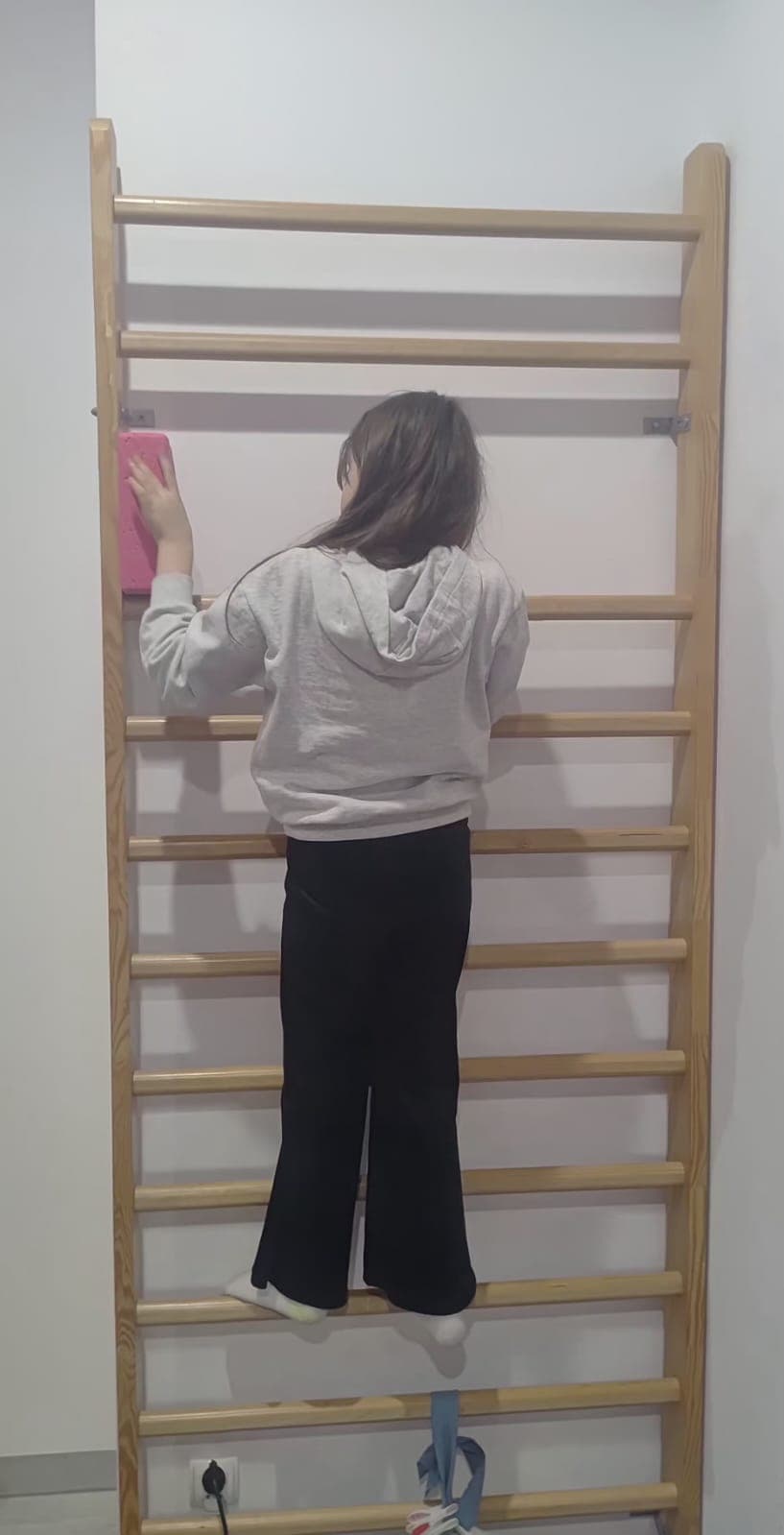 Dziecko wykonuje ćwiczenie ruchowe przy drabince w sali terapeutycznej.